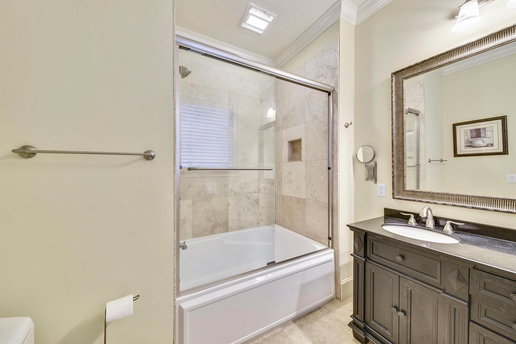 A bathroom with a glass-enclosed shower, a white bathtub, a dark vanity with a large mirror, and a toilet.