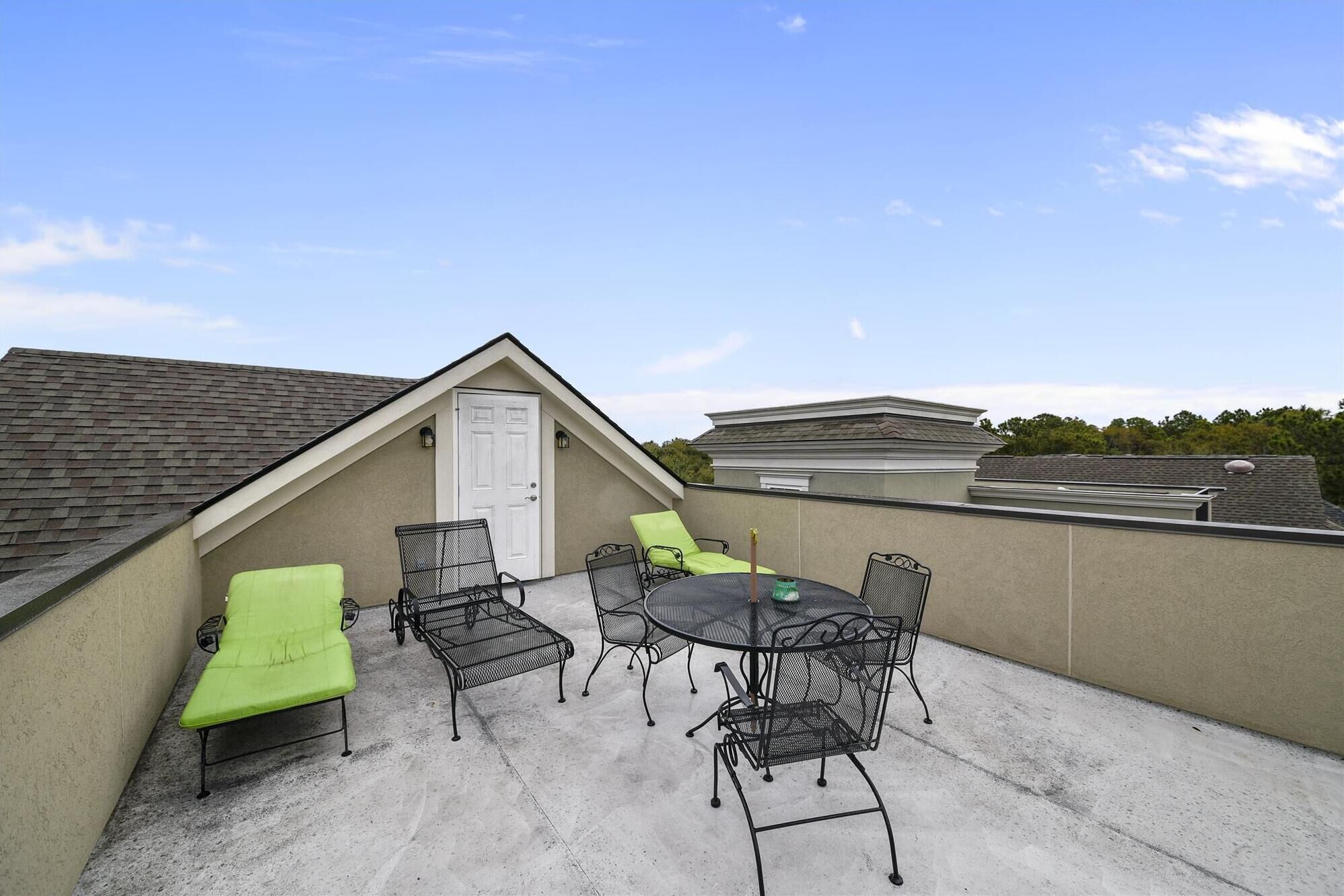 Une terrasse sur le toit avec une table et des chaises, un banc vert rembourré et une porte blanche.