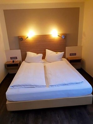 A double bed with a wooden headboard, two bedside tables, and wall-mounted lamps.