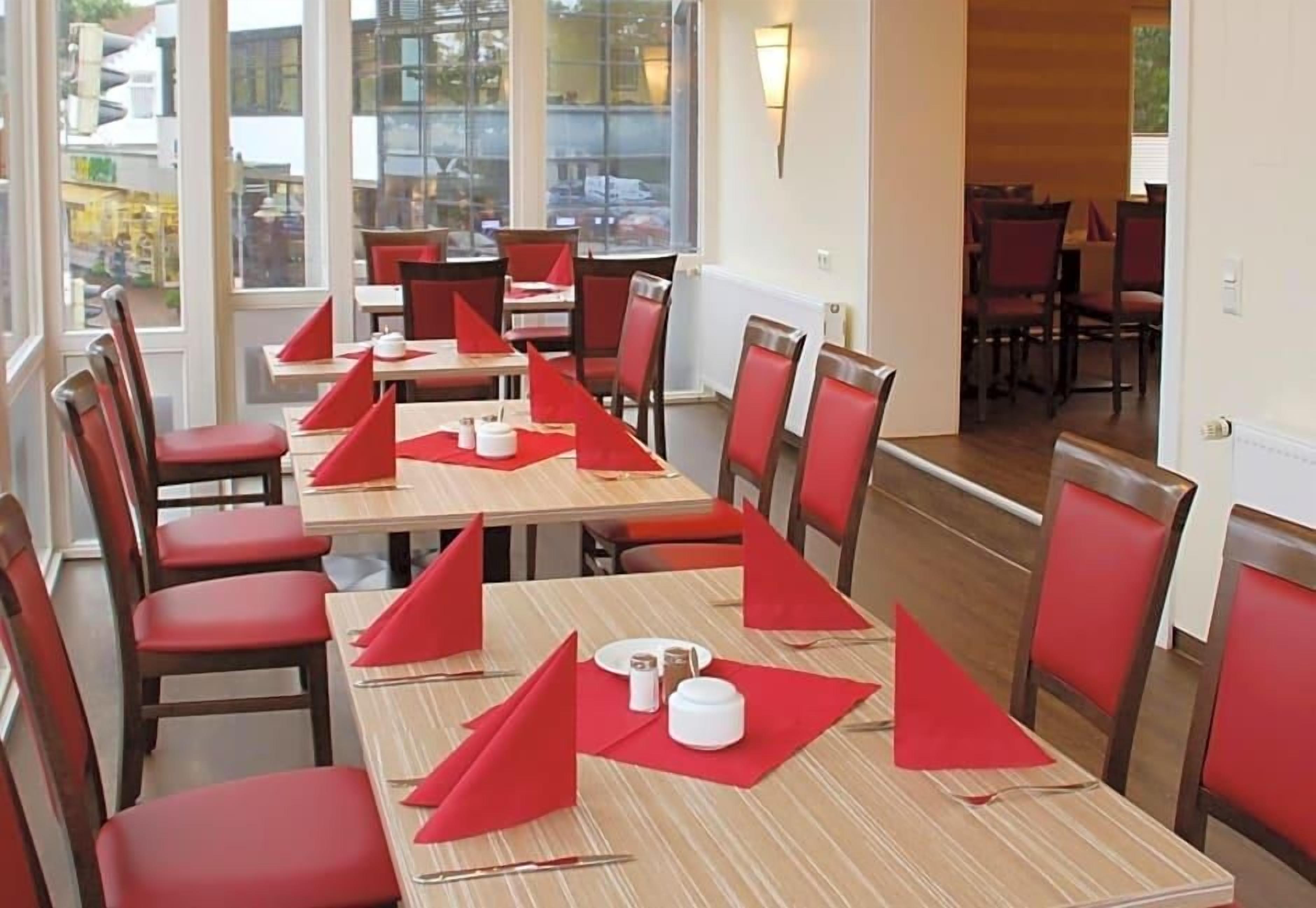 A dining area with tables set for multiple people, chairs, and a view of the outside through large windows.