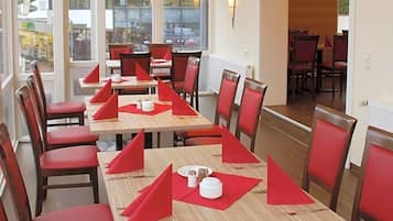 A dining area with tables set for multiple people, chairs, and a view of the outside through large windows.