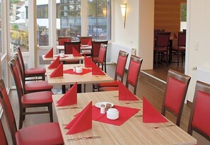 A dining area with tables set for multiple people, chairs, and a view of the outside through large windows. - Hotel Mv Hleneck (Schortens)