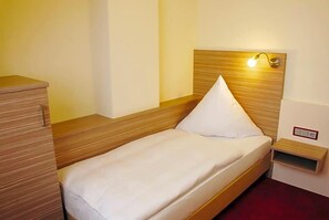 A single bed with a wooden headboard and a bedside table with a lamp.