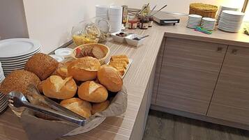 A buffet setup with various breads and pastries, serving trays, and condiments.