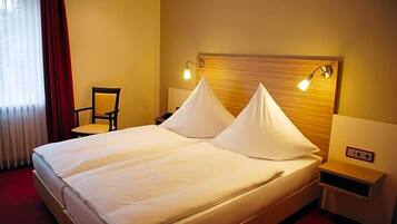 A hotel room with a double bed, two bedside lamps, a chair, and a nightstand.
