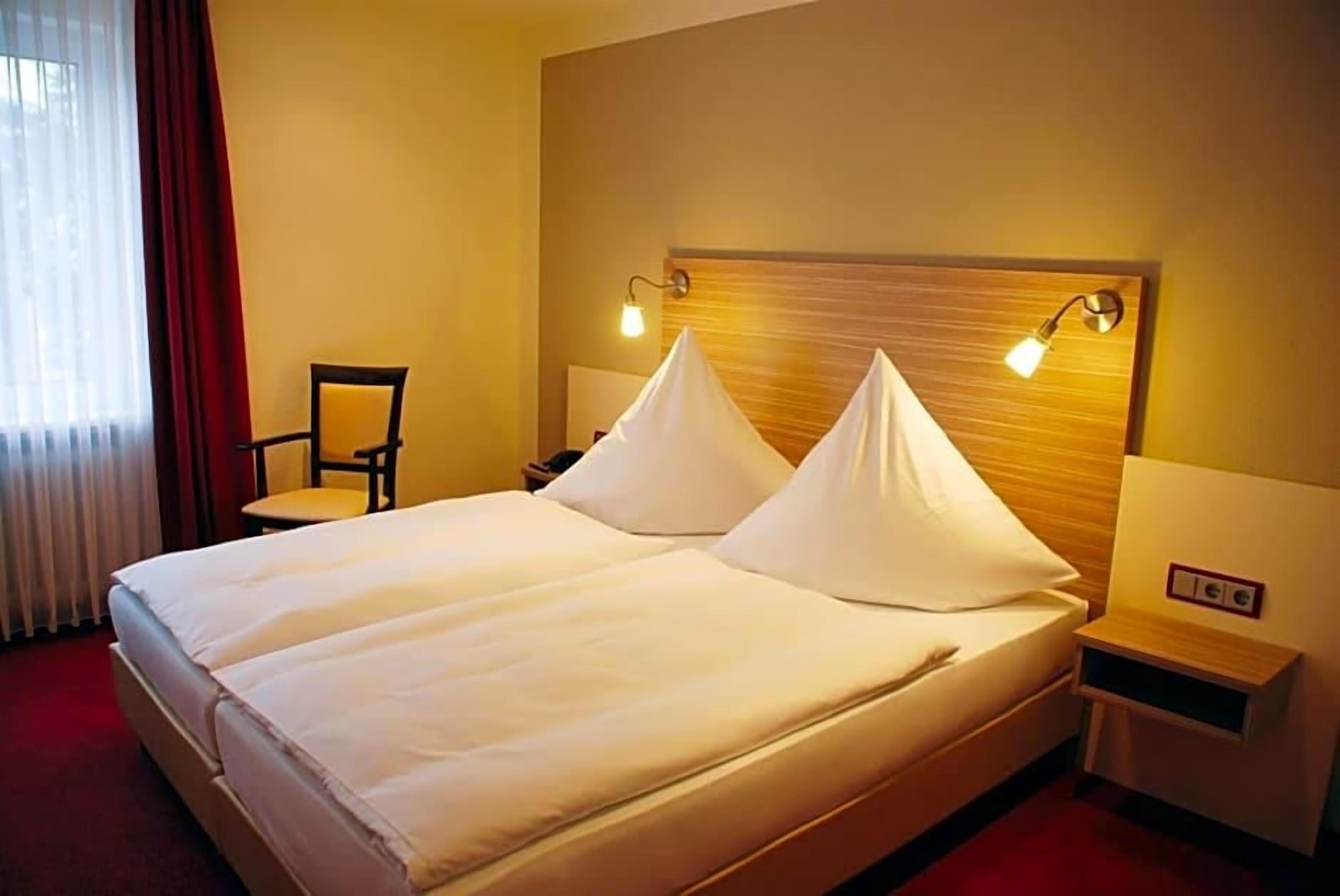 Une chambre d’hôtel avec un lit double, deux lampes de chevet, une chaise et une table de chevet.