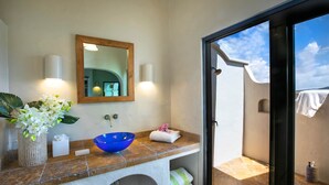Une salle de bain avec un plan de toilette en pierre, un lavabo bleu, un miroir et une vue sur l’extérieur grâce à une porte en verre.