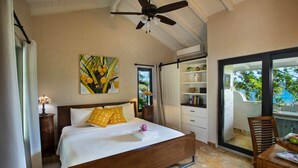 Une chambre à coucher comprenant un lit, un ventilateur de plafond, un tableau, une table de chevet, une lampe, une fenêtre, une porte coulissante, une chaise et une table.