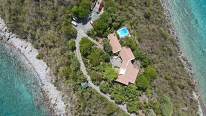 Vue aérienne d’une propriété située sur la côte, avec une piscine, plusieurs b âtiments et une route sinueuse.