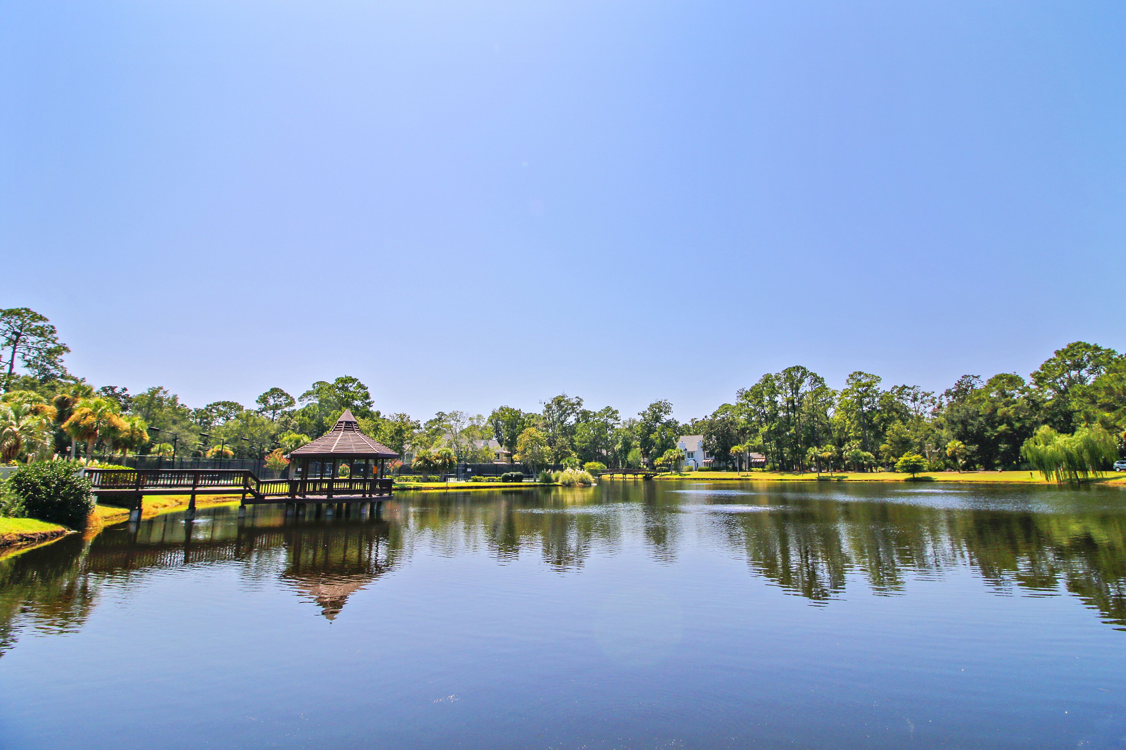 A tranquil lake with a wooden bridge and gazebo, surrounded by lush greenery and trees.