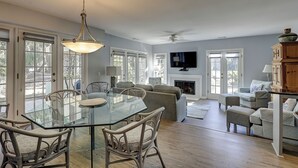 A spacious living room with a glass-top dining table, wicker chairs, a fireplace, and a television mounted on the wall. - Sunset Rentals | Evian 156 (Hilton Head Island)