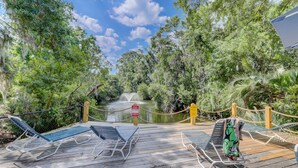 Une terrasse en bois avec des chaises longues donnant sur un bassin d’eau et une végétation luxuriante.