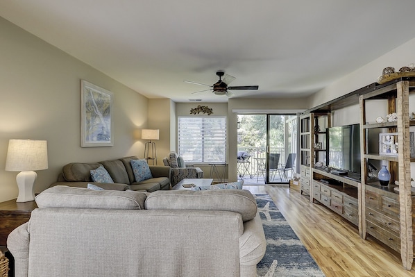 A living room with a sofa, a coffee table, a TV stand, and a ceiling fan.