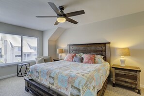 A bedroom with a bed, two bedside tables with lamps, a ceiling fan, and a window with blinds.
