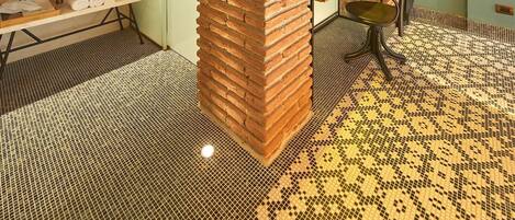Una habitación con un arco de ladrillo, un tocador blanco con espejo, una mesa amarilla y un piso estampado.