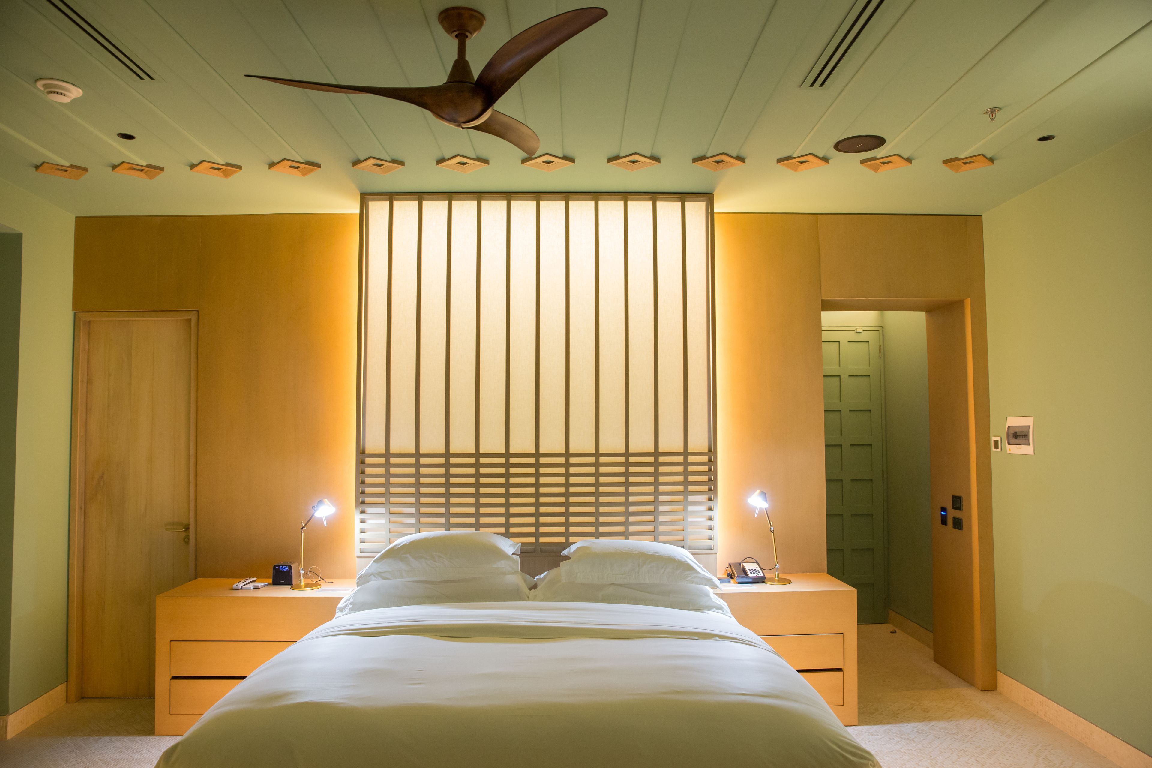 Een slaapkamer met een bed, nachtkastjes, een plafondventilator en een schuifdeur.