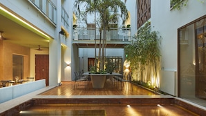 A spacious indoor courtyard with a wooden floor, a central seating area with tables and chairs, and a large potted plant. - Hotel Casona del Colegio (Cartagena)