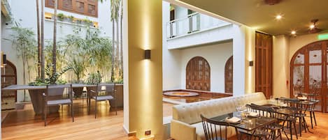A spacious indoor area with a wooden floor, a sofa, dining tables, and chairs.
