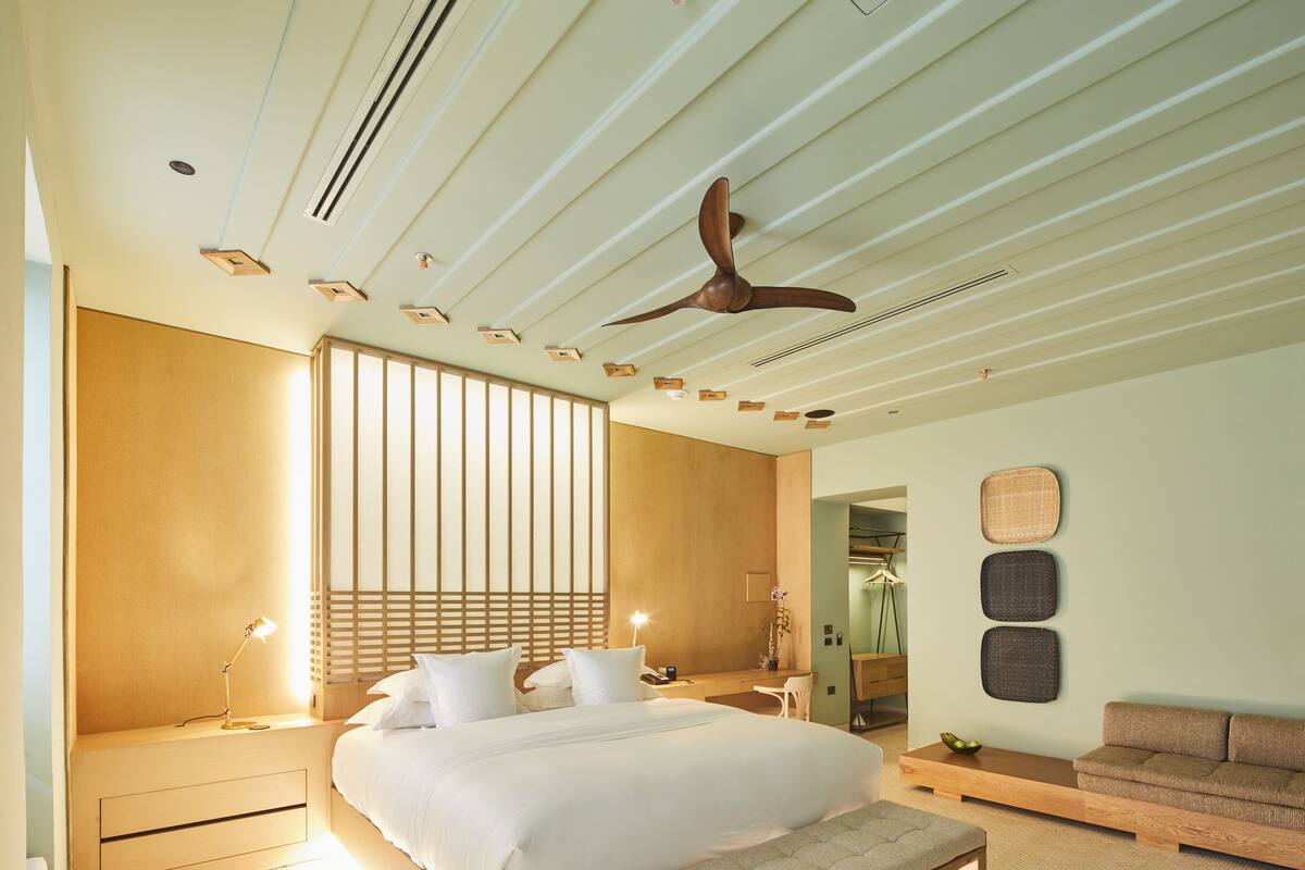 Ein modernes Schlafzimmer mit einem großen Bett, Nachttischen, einer Bank, einem Deckenventilator und einem an der Wand montierten Regal.