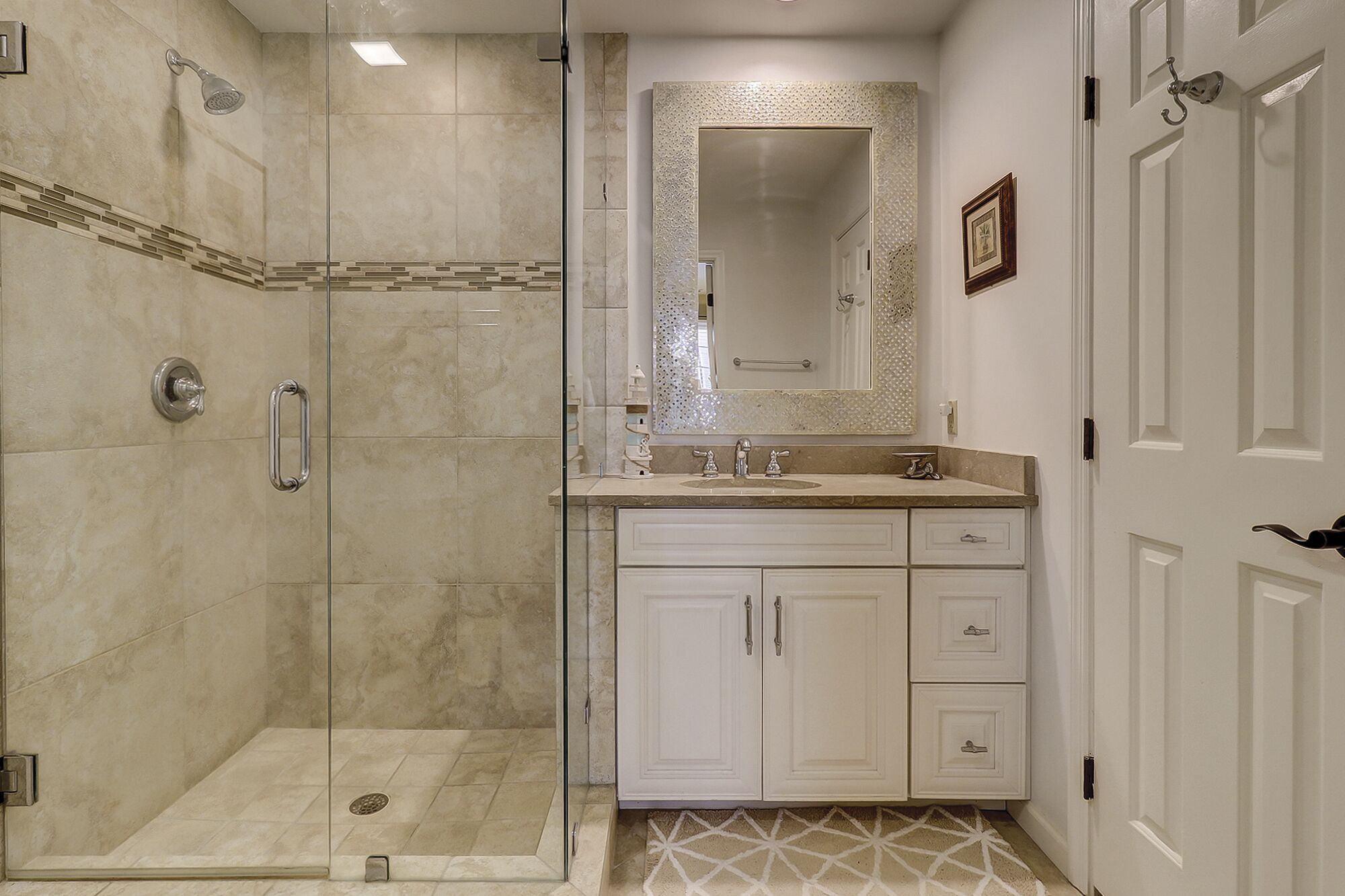 Une salle de bain avec une douche à l’italienne, un meuble-lavabo avec un miroir et une porte dotée d’une poignée.