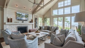 A spacious living room with a fireplace, comfortable seating, and large windows offering a view of the sea. - Sunset Rentals | Duck Hawk 27 (Hilton Head Island)