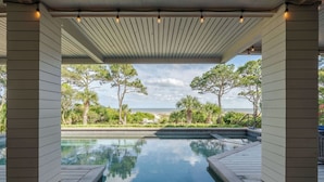 A pool area with a clear view of the ocean, surrounded by trees and a covered patio. - Sunset Rentals | Duck Hawk 27 (Hilton Head Island)