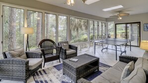 A spacious room with large windows, wicker furniture, a table, and ceiling fans. - Sunset Rentals | Mooring Buoy 175 (Hilton Head Island)