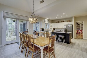 A spacious kitchen with a dining area, featuring a large island, wooden chairs, and a chandelier.