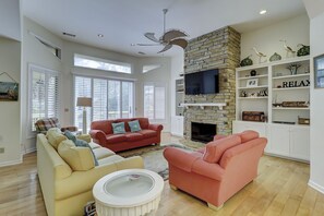 A spacious living room with a stone fireplace, a flat-screen TV, and a bookshelf.