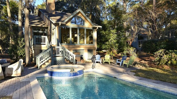 A pool area with a hot tub, outdoor seating, and a house with a porch. - Sunset Rentals | Gloucester 79 (Hilton Head Island)