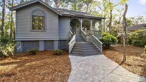 A two-story house with a front porch, a staircase, and a brick pathway leading to the entrance. - Sunset Rentals | Gloucester 79 (Hilton Head Island)