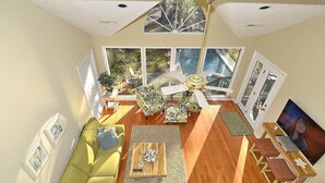 A spacious living room with a green sofa, a wooden coffee table, a ceiling fan, and large windows offering a view of the outdoors. - Sunset Rentals | Gloucester 79 (Hilton Head Island)