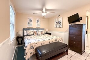 Une chambre à coucher comprenant un lit, un banc, une commode, un téléviseur et des œuvres d’art accrochées aux murs.