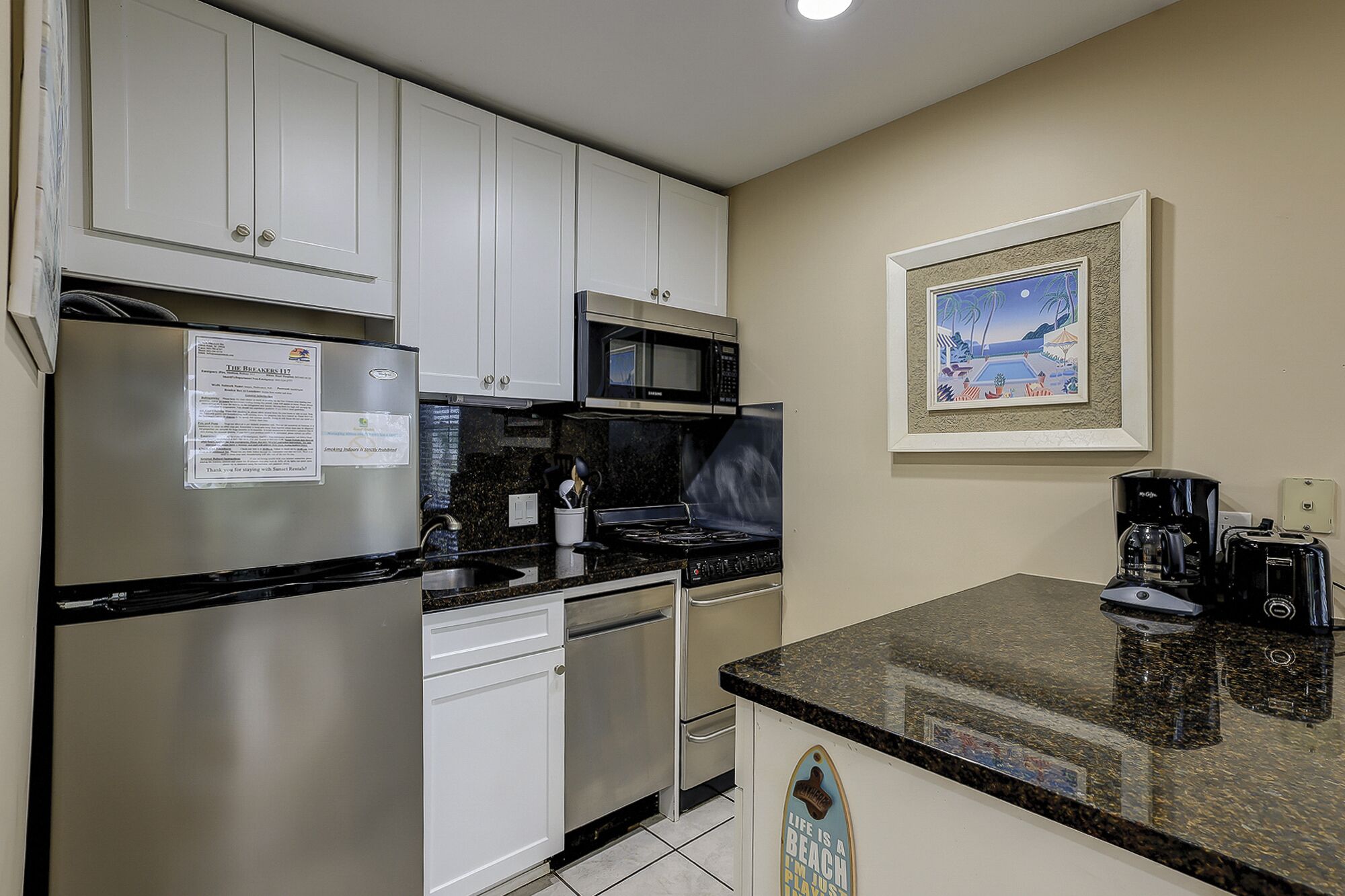 A kitchen with white cabinets, a stainless steel refrigerator, a microwave, a stove, and a coffee maker.
