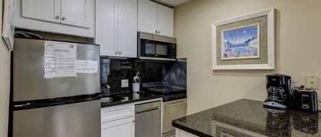 A kitchen with white cabinets, a stainless steel refrigerator, a microwave, a stove, and a coffee maker.