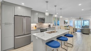 A modern kitchen with grey cabinets, stainless steel appliances, and a marble island with blue bar stools.