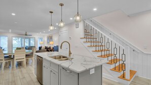 A modern kitchen with a marble island, stainless steel sink, and pendant lighting.