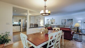 A modern kitchen with stainless steel appliances, a dining area with a wooden table and white chairs, a living room with a sofa and a coffee table, and a hallway leading to another room. - Sunset Rentals | Evian 257 | Dog Friendly (Hilton Head Island)