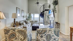 Un vaste salon comprenant un ensemble de canapés, des fauteuils à motifs, un ventilateur de plafond et un escalier menant à un niveau supérieur.