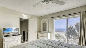 Une chambre à coucher comprenant un lit, une commode, un téléviseur et une grande fenêtre donnant sur la plage.