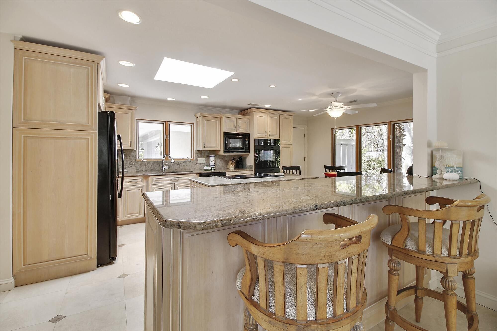 A spacious kitchen with a large island, wooden chairs, and a view of the outdoors.