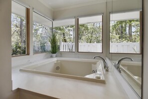 A modern bathroom with a large bathtub, two sinks, and large windows offering a view of a white fence and trees. - Sunset Rentals | Off Shore 63 | Dog Friendly (Hilton Head Island)