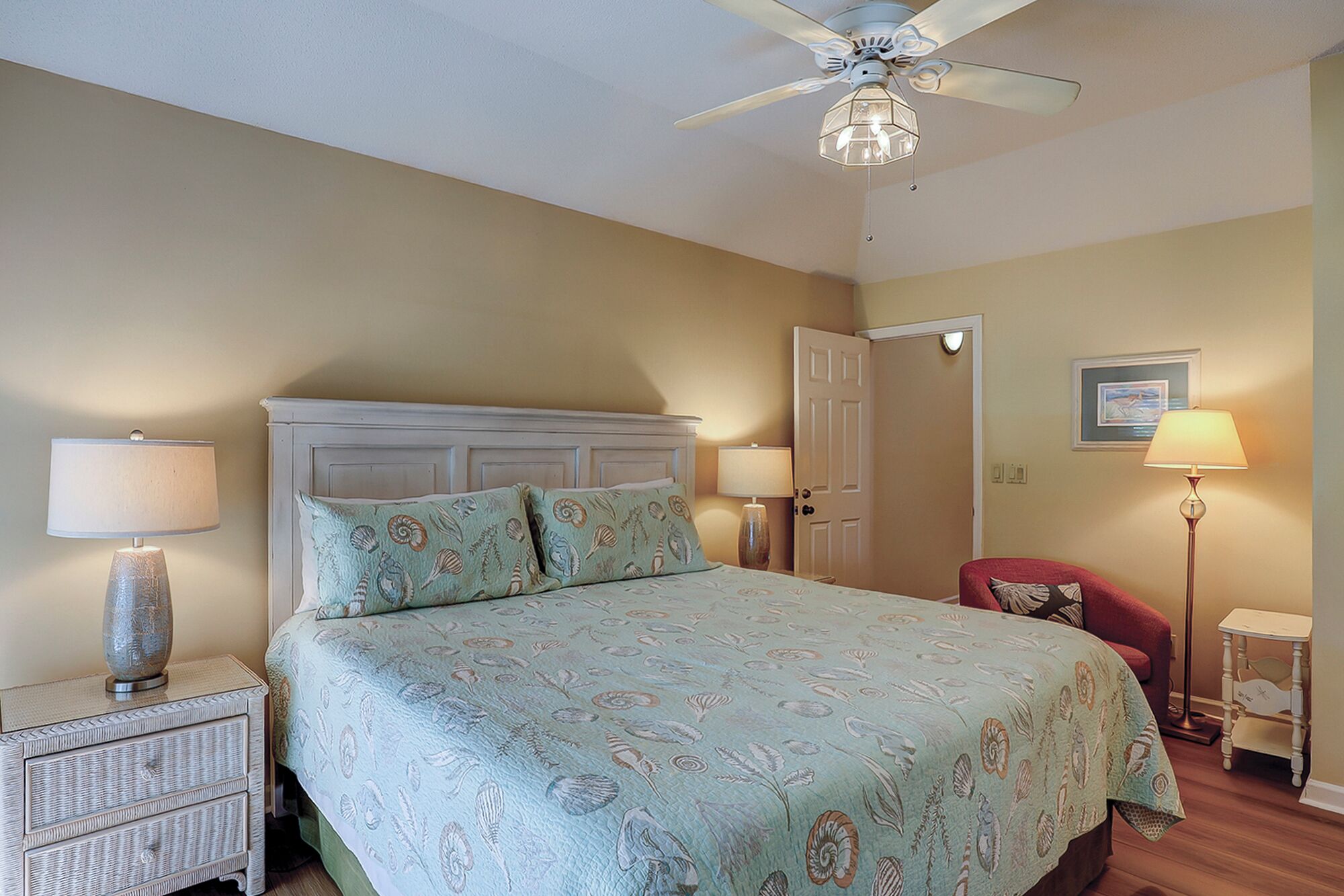 A bedroom with a bed, two bedside tables, a ceiling fan, a door, and a chair.
