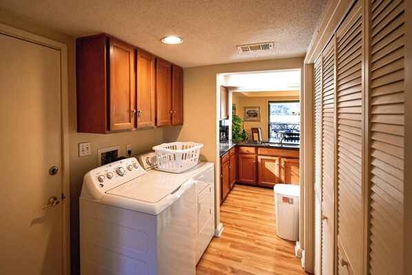 A laundry area with a washer and dryer, wooden cabinets, and a view to the outside.