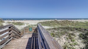 Ein hölzerner Steg führt zu einem Strand mit freiem Blick auf das Meer und Strandstühlen.