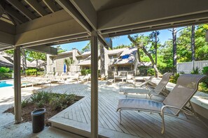 A covered outdoor area with a pool, lounge chairs, and a wooden deck.