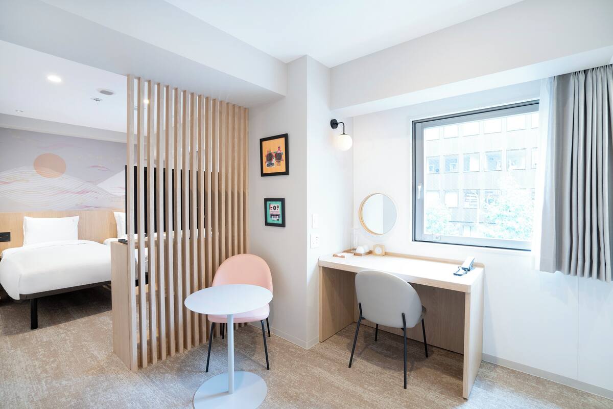A modern hotel room with a bed, desk, chair, and a large window.