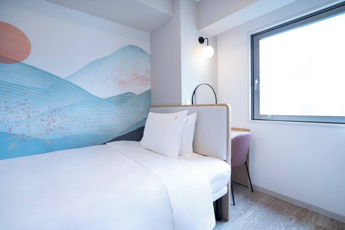 A modern hotel room with a bed, a desk, and a large window.
