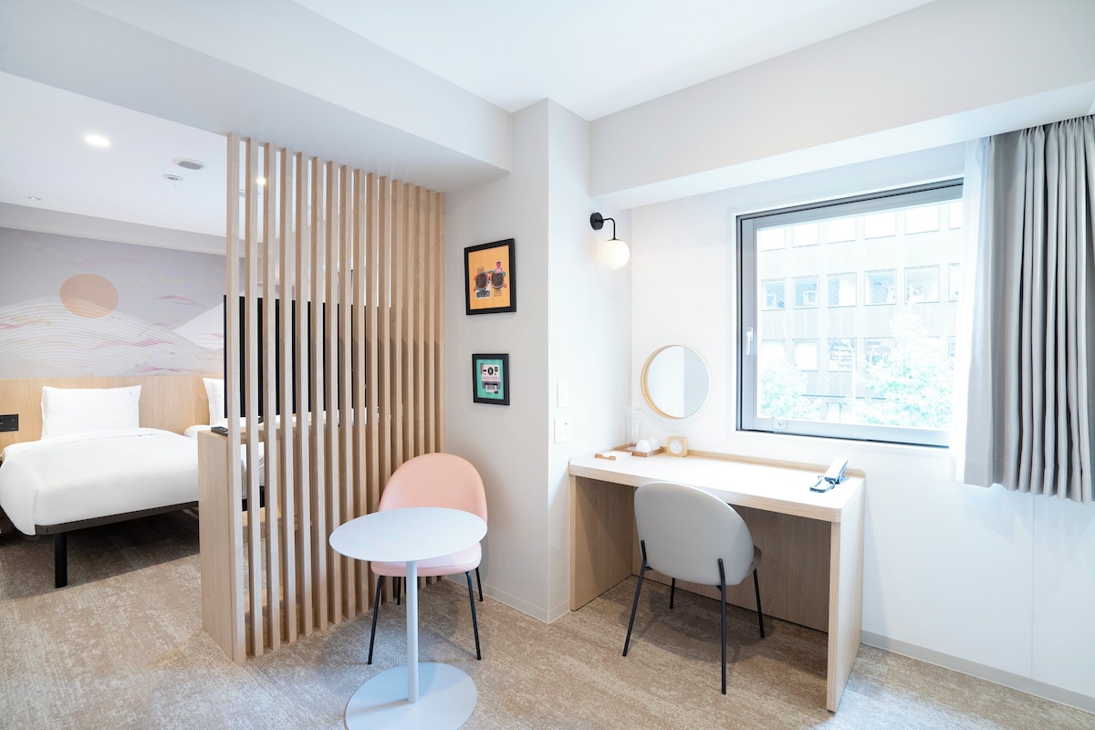 Una habitación de hotel moderna con cama, escritorio, silla y un amplio ventanal.