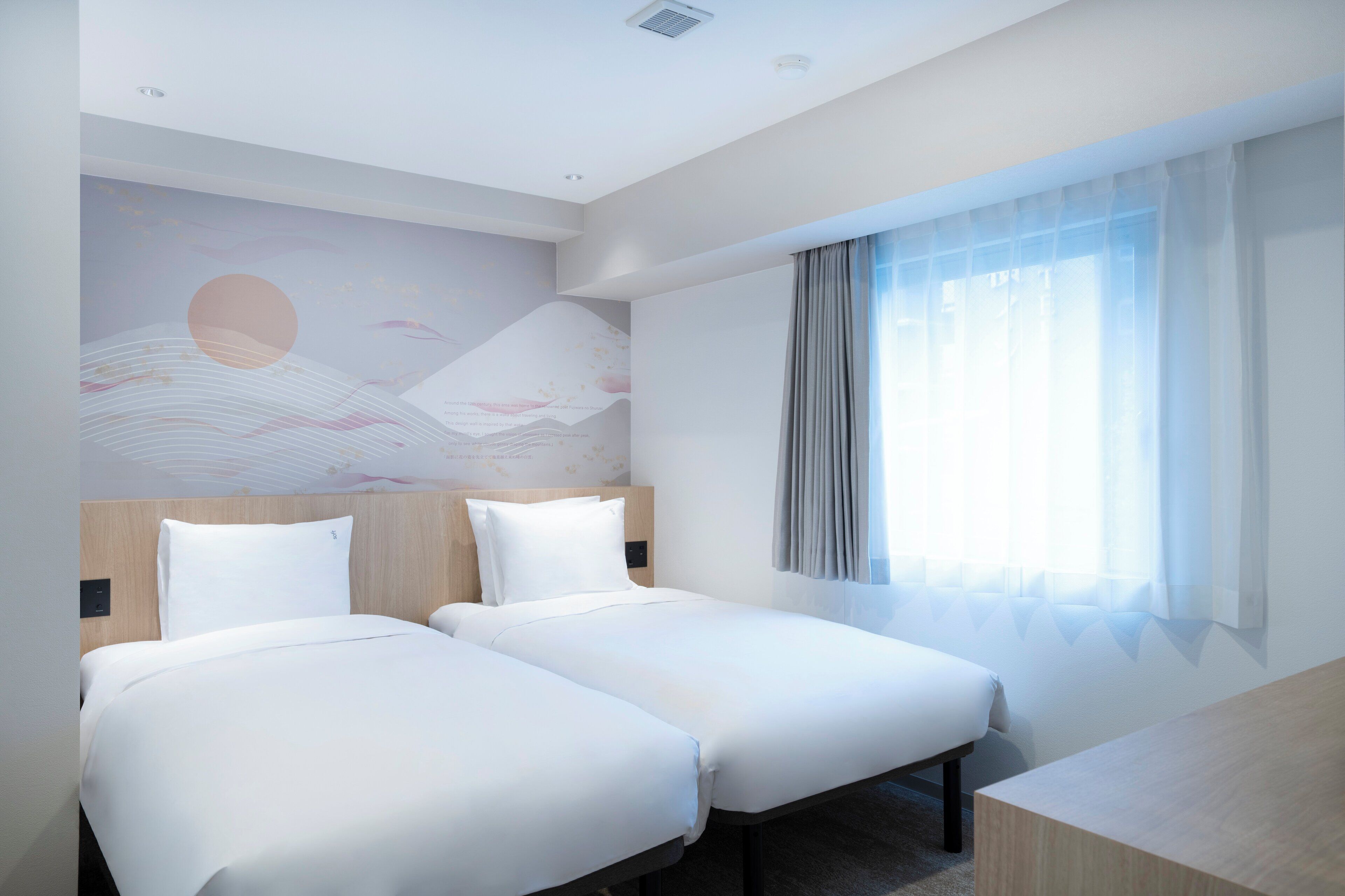 A hotel room with two single beds, a wooden headboard, a large window with sheer curtains, and a wall mural.